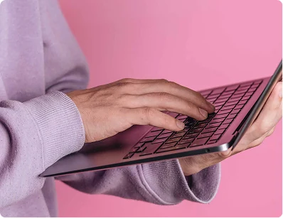 Hands typing on a laptop on a pink background