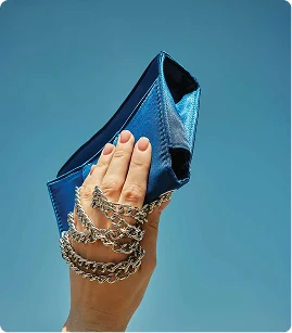 Hand holding a chained clutch bag on a blue background