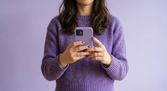 Person in a purple sweater holding a phone on a purple background